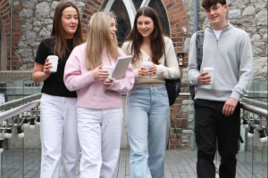 Four students walking together with notebooks and drinks ahead of starting college