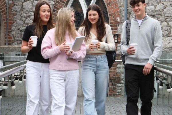 Four students walking together with notebooks and drinks ahead of starting college