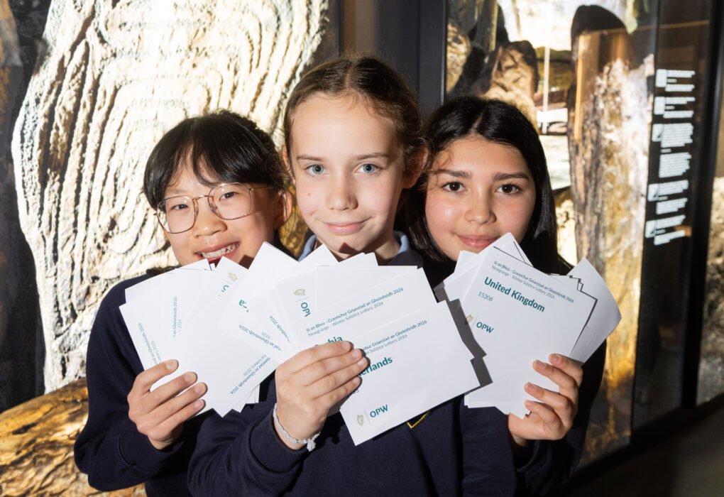 Three schoolchildren holding entries during the 2026 Newgrange Winter Solstice lottery draw at Brú na Bóinne