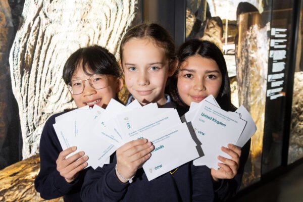 Three schoolchildren holding entries during the 2026 Newgrange Winter Solstice lottery draw at Brú na Bóinne