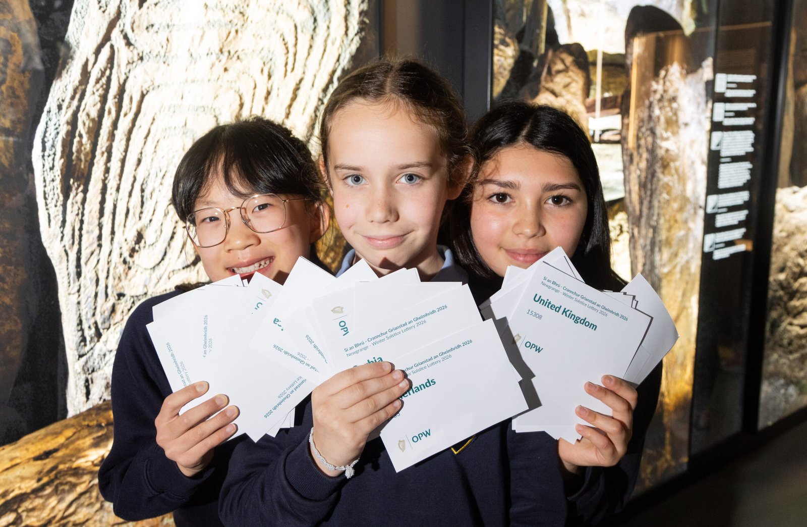 Three schoolchildren holding entries during the 2026 Newgrange Winter Solstice lottery draw at Brú na Bóinne